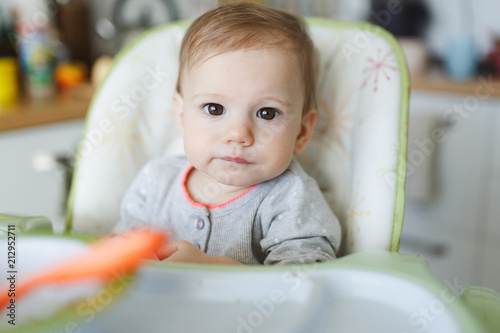 Portrait of adorable baby girl eating at home sitting at baby table.