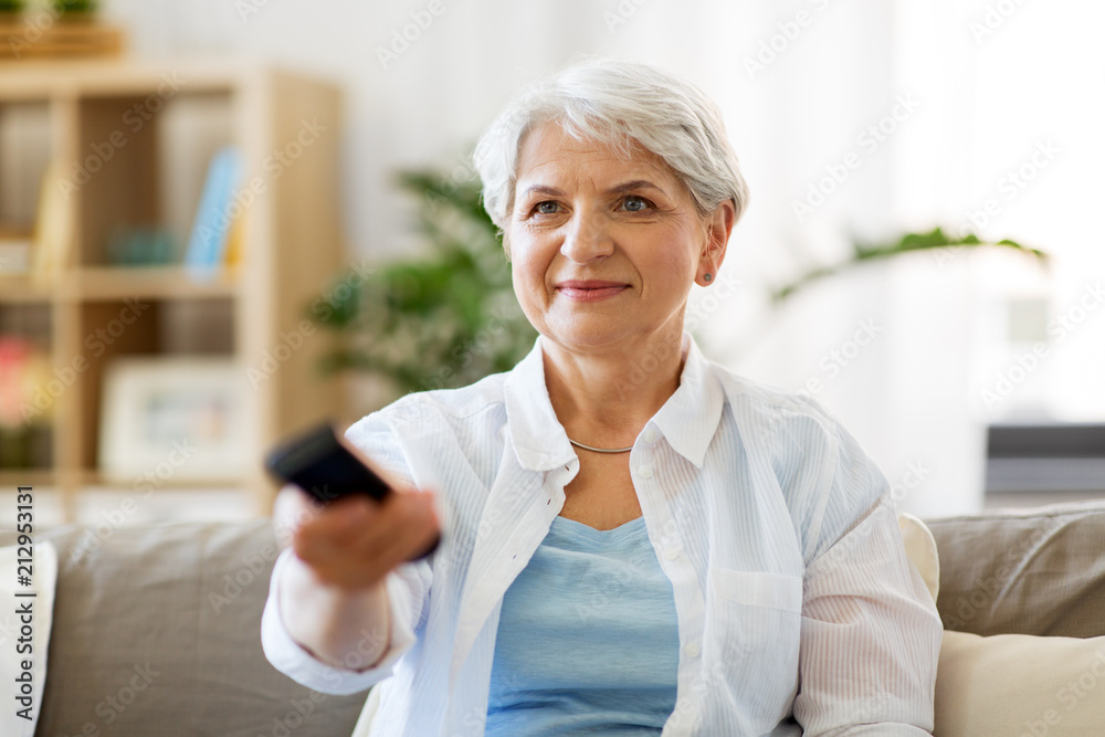 people, television and entertainment concept - senior woman in eyeglasses with remote control watching tv at home people, television and entertainment concept - senior woman in eyeglasses with remote control watching tv at home