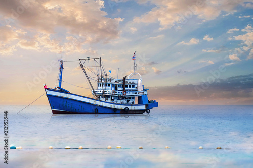 Fotografiet Blue - White Fishing Boat In The Sea And Dramatic Clouds At Sunrise
