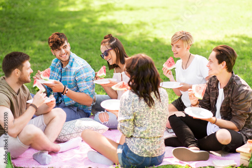 friendship, leisure and summer concept - group of happy friends eating watermelon at picnic in park