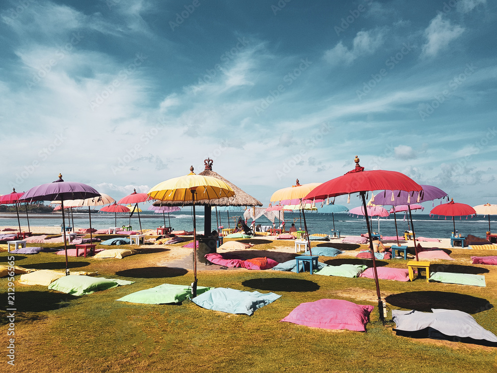 Fototapeta premium Colorful umbrellas and big pillows seats on the green grass near to the beach over sea and sky background