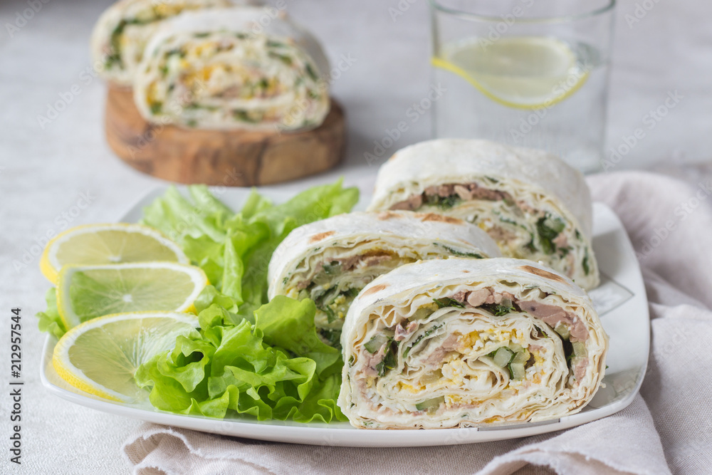 Tuna salad roll sandwich with salad leaves on white plate. Roll sandwich with tuna, cucumber, eggs and dill. Thin Armenian pita bread or lavash. Snack. Tuna salad roll sandwich with salad leaves on white plate. Roll sandwich with tuna, cucumber, eggs and dill. Thin Armenian pita bread or lavash. Snack.