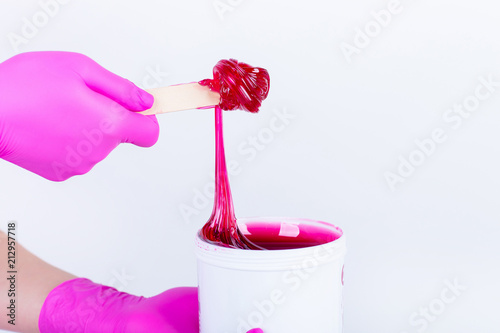 hands in crimson gloves holding a jar with sticky paste for sugaring isolated on white background. photo
