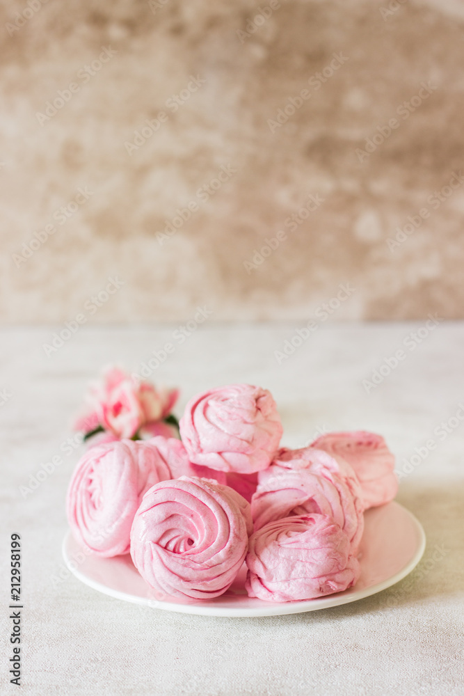 Beautiful delicious dessert. Pink zephyr on a white plate and pink flower. Berry zephyr on light gray background. Beautiful delicious dessert. Pink zephyr on a white plate and pink flower. Berry zephyr on light gray background.