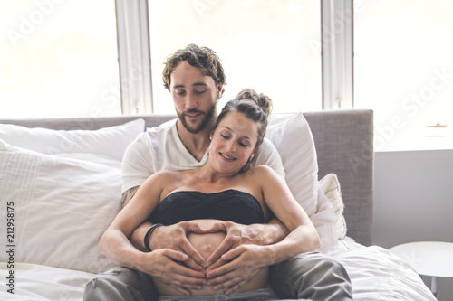 Man with pregnant woman in bed at home having great time