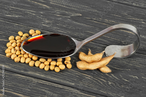 Soybeans and soy sauce in spoon on wooden background