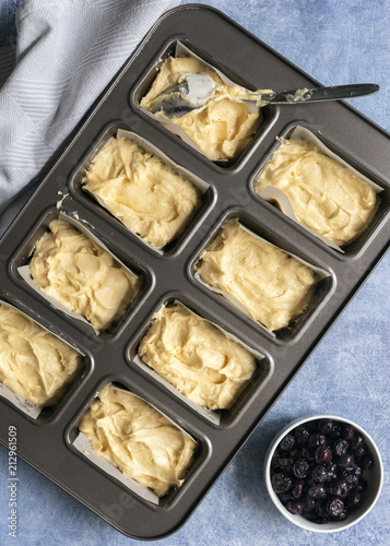 Blueberry cake mixture spooned into a baking tin for individual loaves alongside a bowl of blueberries. photo