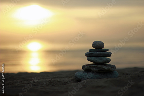 Focused balanced cairns on beach in front of the sea by sunset/sunrise