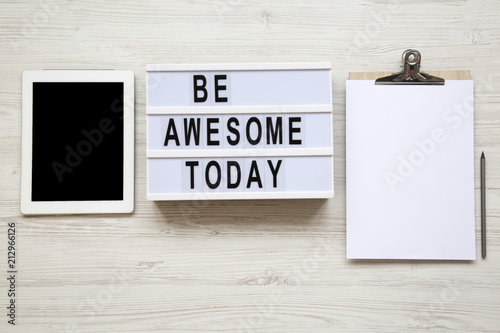 Work space with tablet, notepad and 'Be awesome today' word on lightbox over white wooden background, top view. From above, flat-lay, overhead. photo