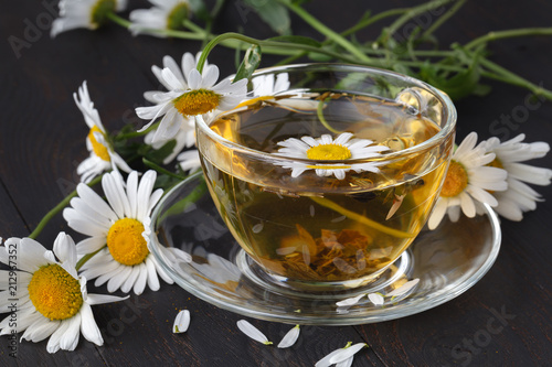 Cup of chamomile tea with chamomile flowers on wooden planks