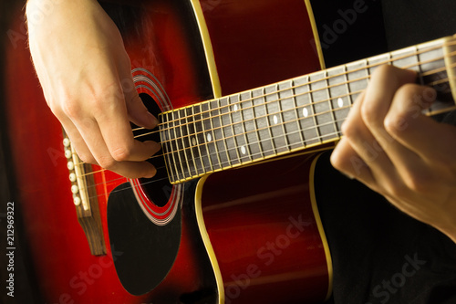 Acoustic guitar red, dark background, sits the musician playing on classical Spanish, musical school game for children and adults close-up of fingerboard and strings, the soundboard of the instrument