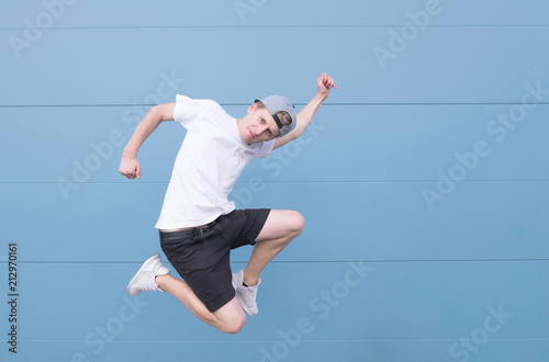 Portrait of a young man in a white T-shirt tv in the air on a blue background. Young man jumping against the background of a blue-haired wall. Levitation on a blue background