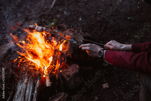 Man traveler fry sausages on fire in the woods. Evening light. Environment and nature concept.