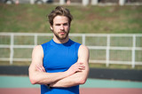Focused on sport achievement. Confident athlete sportsman. Man blue sport clothing stadium background. Athlete confident holds hands crossed. Man athlete muscular arms ready for training outdoors