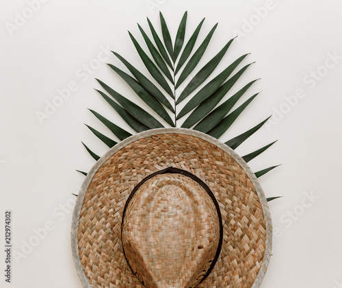Flat lay with straw hat and leaf of tropical palm leaf on pastel background. Minimal styled composition