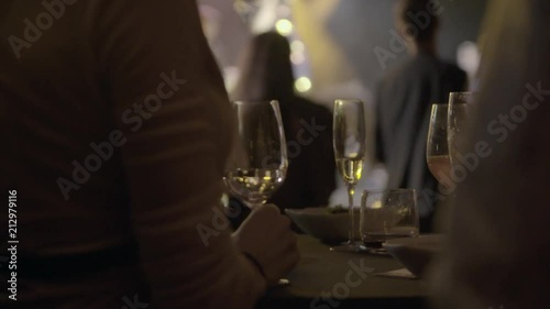 Waiter served champagne glasses on a tray in a fine dining restaurant during concert with bright spotlights in the background.