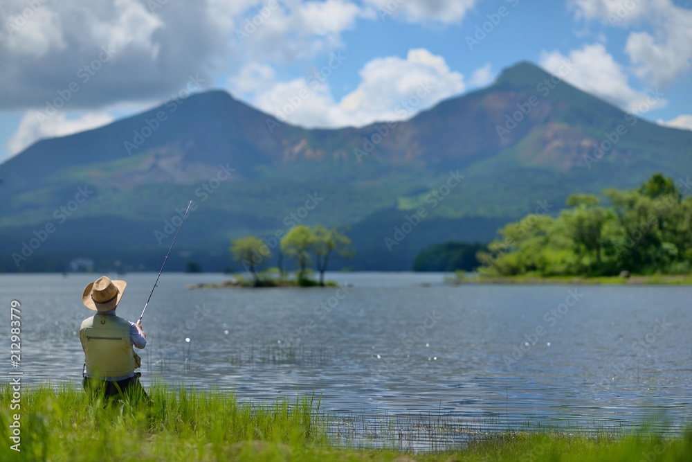 夏の湖畔・のんびりと釣りをする男性 