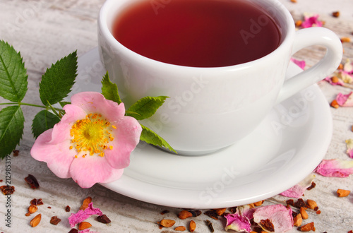 Cup of tea with wild rose flower on old rustic plank