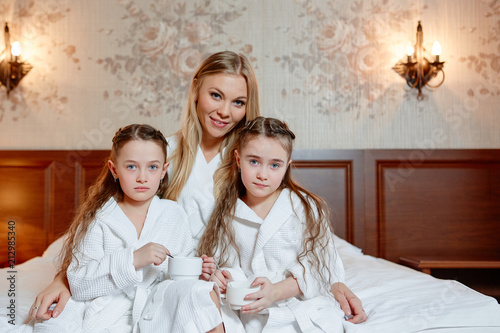 The happy family, mother and daughters twins, sit and relax on a bed in the cozy room