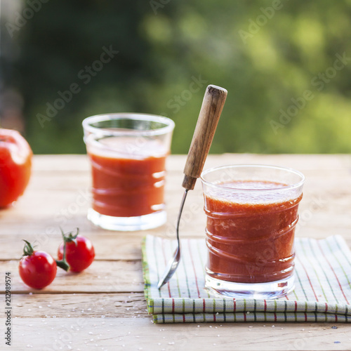 Delicious homemade tomato juice with salt on a striped napkin on a wooden table on a green foliage background. Selective focus. Close up.