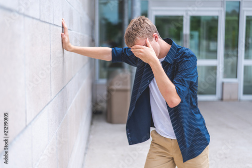 Upset teen leaning against a brick wall outside of a public building.