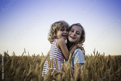 Foto Two girls smiling and hugging in the wheat