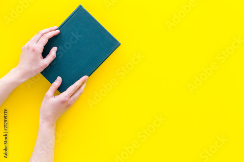 Reading concept. Reading as hobby. New knowledge. Hands take hardback book with empty cover on yellow background top view copy space