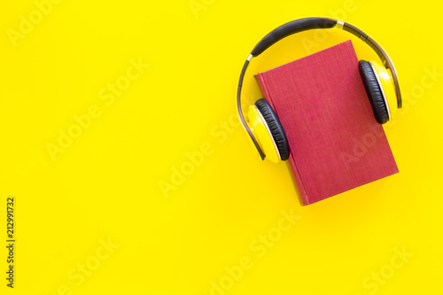 Audiobooks concept. Headphones put over hardback book with empty cover on yellow background top view copy space