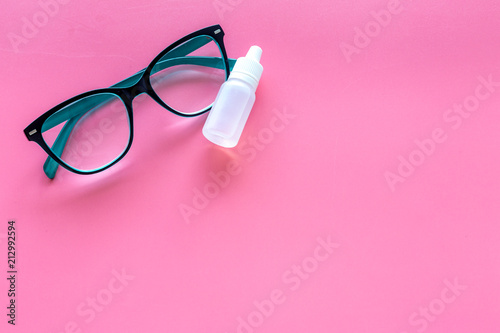 Eye drops in small bottle near glasses on pink background top view copy space
