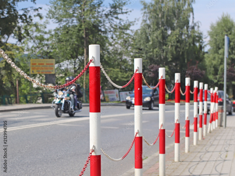 The designation of traffic signs for the separation of pedestrian and transport zones for traffic safety. Red and white markings. Handrail with chain. Traffic on the road. Motorcycle and cars. The designation of traffic signs for the separation of pedestrian and transport zones for traffic safety. Red and white markings. Handrail with chain. Traffic on the road. Motorcycle and cars.