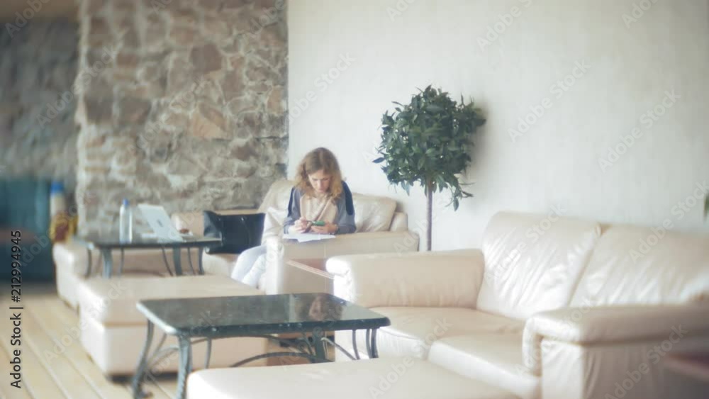 Young beautiful business woman sitting on sofa at table with tablet and using smartphone Young beautiful business woman sitting on sofa at table with tablet and using smartphone