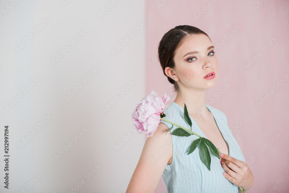 A young woman with gathered hair is standing holding a peony in her hands. A young woman with gathered hair is standing holding a peony in her hands.