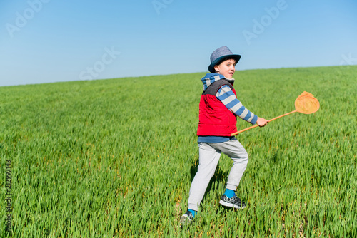 Little boy with a butterfly net in hand runs across the green field. photo