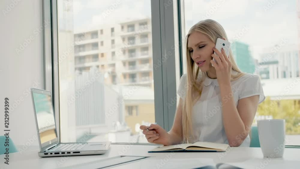 Serious woman working in light office room. Elegant modern businesswoman with laptop and papers at long table in conference light room having phone call. Serious woman working in light office room. Elegant modern businesswoman with laptop and papers at long table in conference light room having phone call.