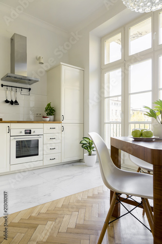 White chair at wooden dining table in simple kitchen interior with window. Real photo