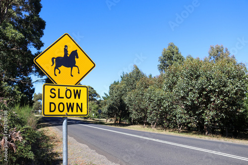 Fototapeta Naklejka Na Ścianę i Meble -  a black and yellow Slow Down, Horse Riders warning sign near a stretch of road