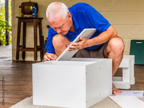 Elderly man fitting a wooden panel to a flat-pack cabinet. photo