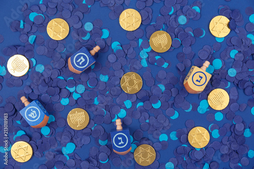 Dark blue background with multicolor dreidels and chocolate coins on blue confetti. Hanukkah and judaic holiday concept.