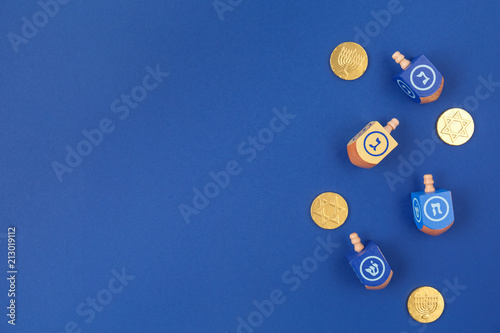 Dark blue background with multicolor dreidels and chocolate coins. Hanukkah and judaic holiday concept.