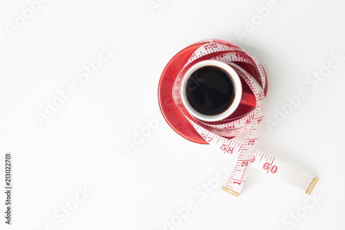 Creative flat lay of healthy and Diet concept with black coffee in red cup and measuring tape on white background with copy space