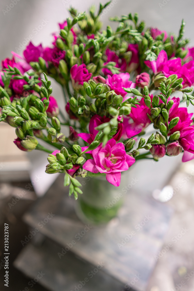 bright pink freesia flowers in glass vase on wooden table. Beautiful summer bouquet. Arrangement with mix flowers. The concept of a flower shop. Content for the catalog