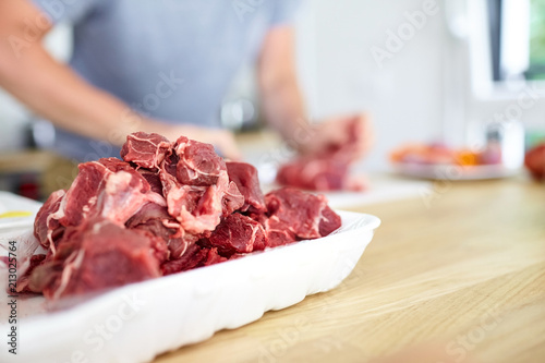 Cooking. Pieces of red chopped meat in a white plastic tray. Second plan: men's hands chef. Selective focus. Blurred background