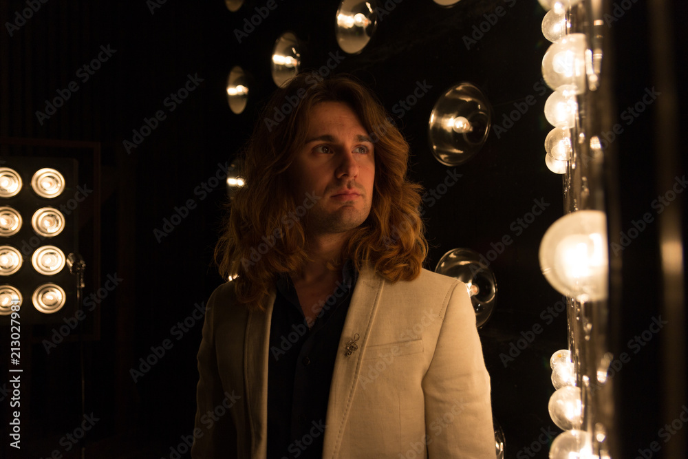 Φωτογραφία a man in a white jacket and in a black shirt, with long hair, stands against the backdrop of bright lanterns, safites