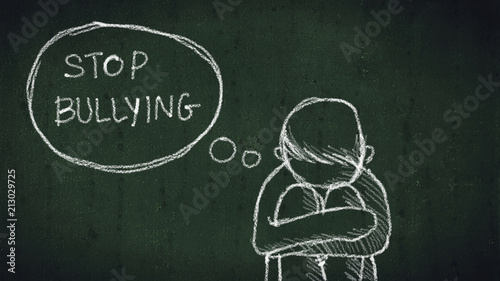sad young boy sitting on the floor with text stop bullying written with chalk on chalkboard. social problems of humanity photo