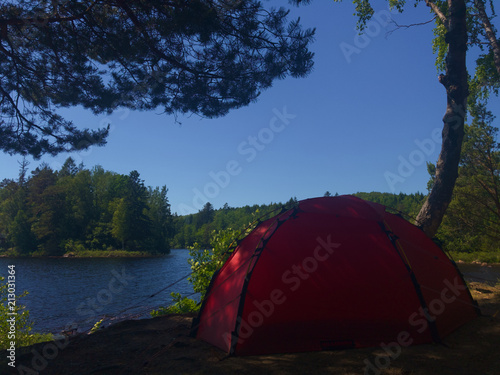 Camping and hiking setup in a forest near a lake with red tent in Sweden during summer