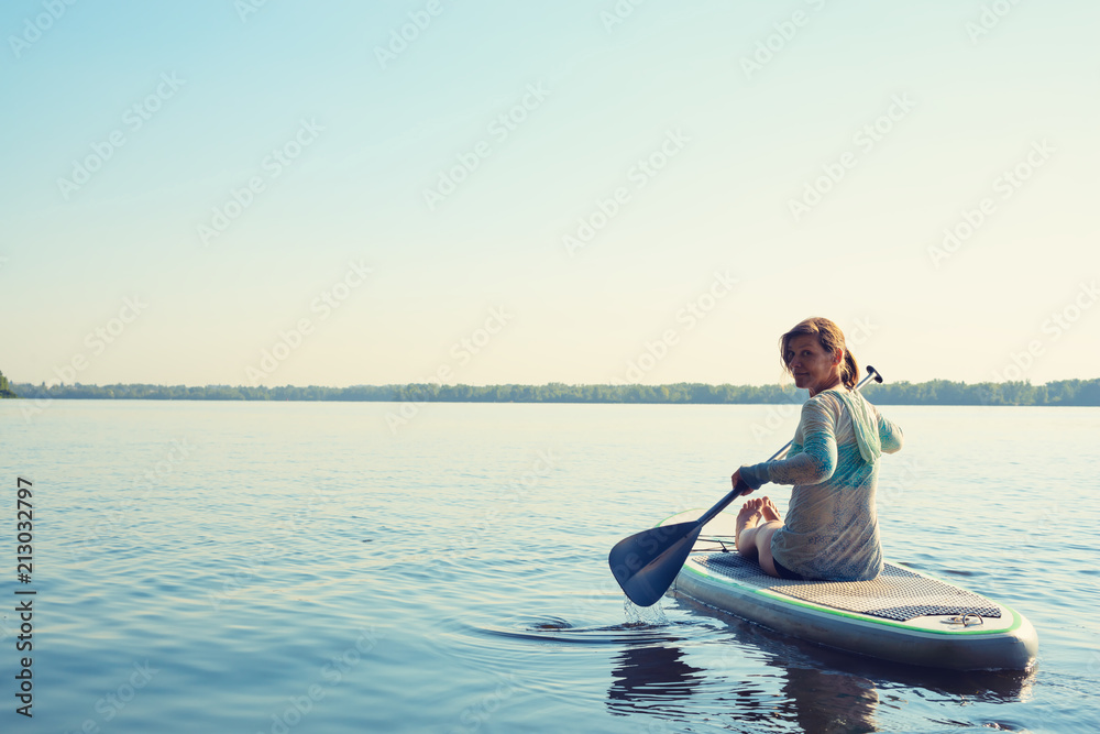 Fototapeta premium Smiling female relaxing on a SUP board and enjoying life