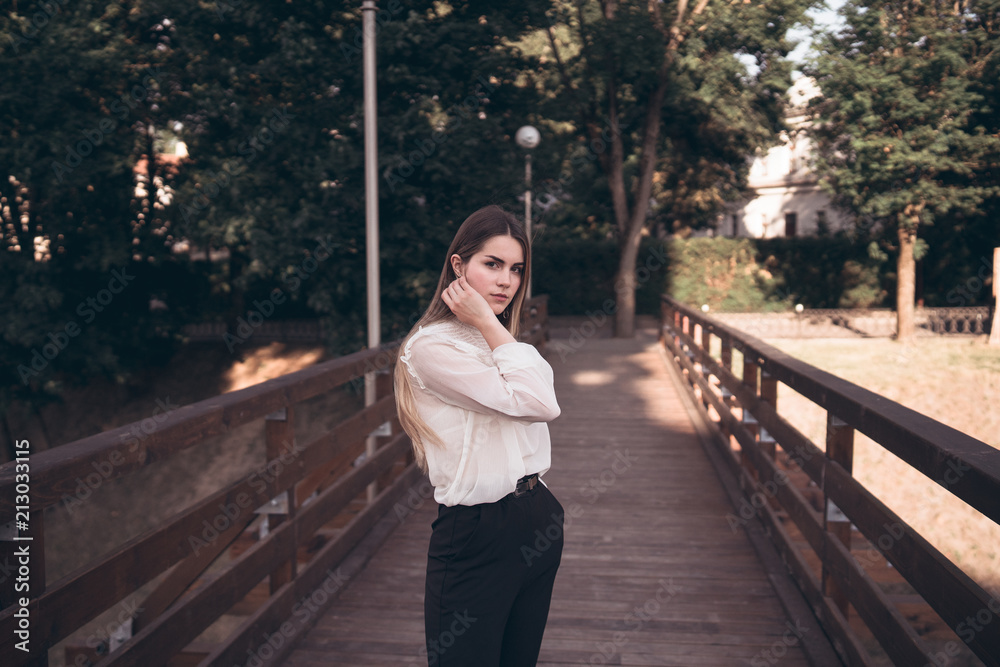  portrait of a beautiful dark-haired girl in a forest park in a white shirt and dark trousers