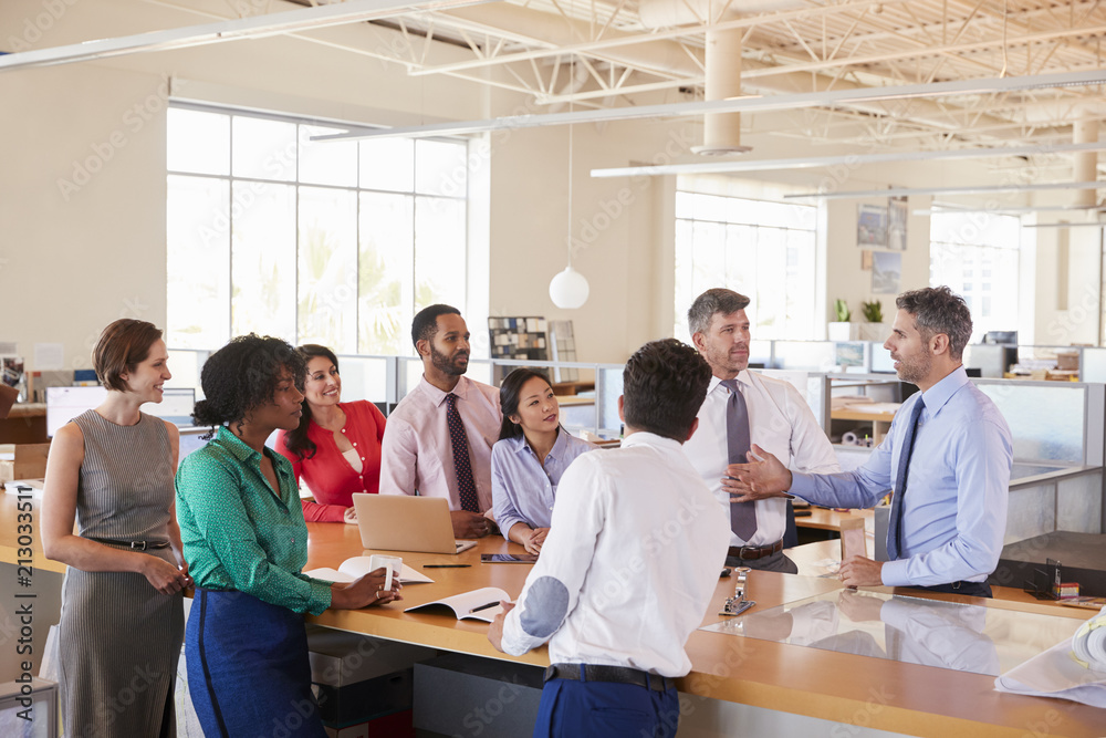 Businessman addressing team at a meeting in open plan office Businessman addressing team at a meeting in open plan office