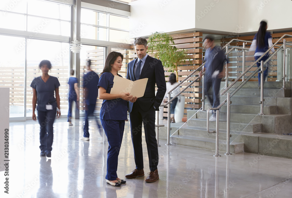 Two healthcare workers talk in the lobby of a busy hospital