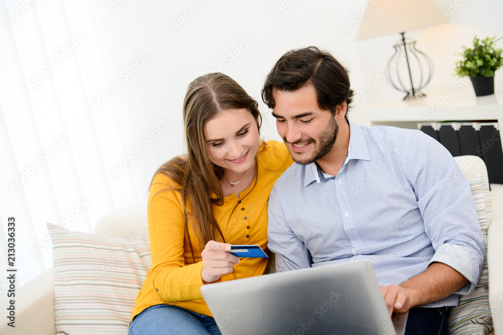 cheerful young couple on sofa at home websurfing and shopping online with credit card, a laptop computer and internet technology cheerful young couple on sofa at home websurfing and shopping online with credit card, a laptop computer and internet technology